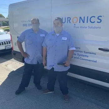 Two employees in uniform standing in front of a Puronics, LLC service van in Livermore.